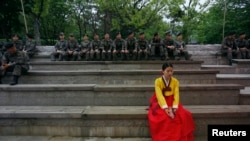 A woman in a traditional Korean Hanbok costume sits in front of South Korean soldiers at Namsangol Hanok Village in Seoul, May 20, 2013. 