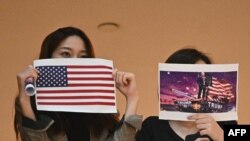 两名香港女子在一个商场内举行的抗议中国人大制定港版国安法的集会上手举美国国旗和川普总统画像。（法新社2020年5月28日）