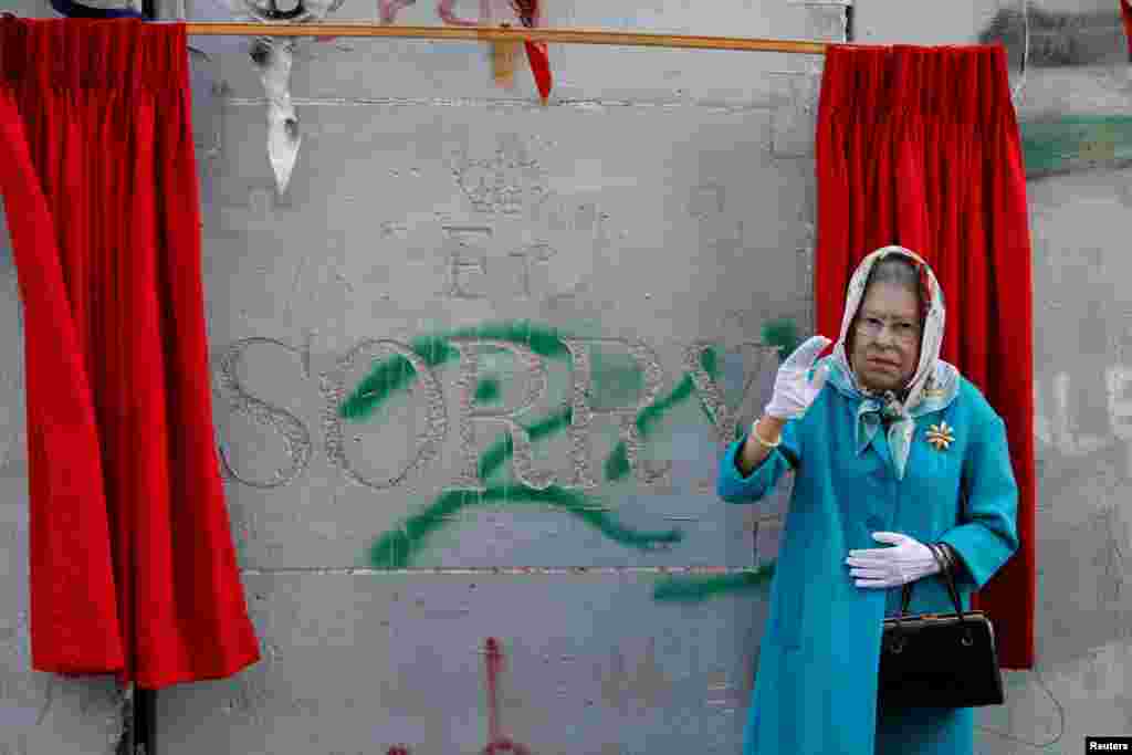 ស្រ្តី​ម្នាក់​ស្លៀកពាក់​ជា​ម្ចាស់ក្សត្រី​អង់គ្លេស Queen Elizabeth II នៅ​ក្នុង​ពិធីមួយ​មុន​នឹង​បុណ្យខួប​ Balfour Declaration​ នៅ​ខាង​ក្រៅ​សណ្ឋាគារ​ Banksy&rsquo;s Walled Off ទីក្រុង​ West Bank នៃ Bethlehem។