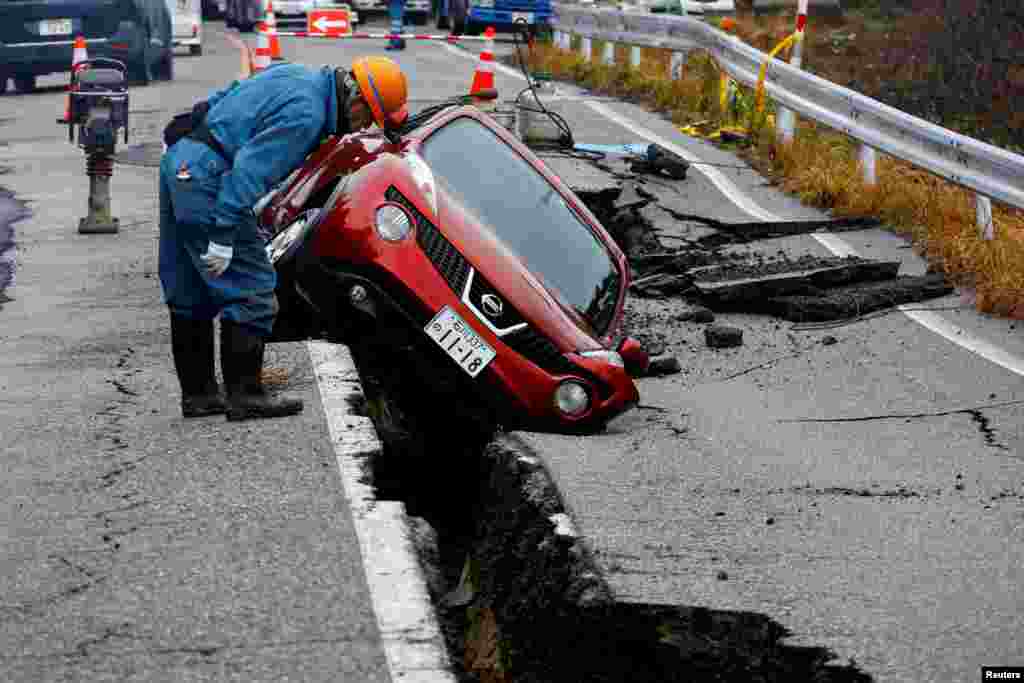 A worker looks at a car stuck on a broken road in the aftermath of an earthquake, near Anamizu, Japan, Jan. 3, 2024.