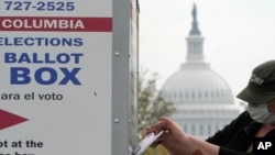 FILE - With the U.S. Capitol dome visible, a voter drops a ballot into an early voting drop box at Union Market in Washington, Oct. 28, 2020.