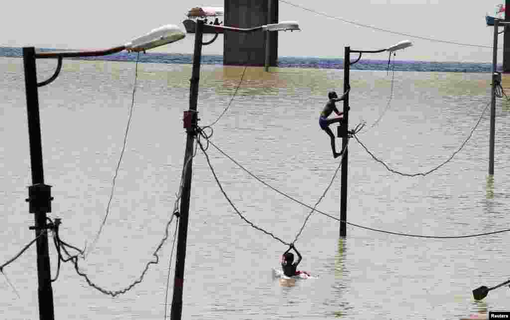Seorang anak memanjat tiang listrik yang sebagian terendam air banjir di tepi sungai Gangga di Allahabad, India.