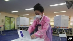 A woman wearing a face mask to help protect against the spread of the new coronavirus casts a vote for the parliamentary elections at a polling station in Seoul, South Korea, Wednesday, April 15, 2020. South Korean voters wore masks and moved slowly…