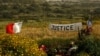 FILE - A banner calling for justice is seen next to a photo of assassinated anti-corruption journalist Daphne Caruana Galizia at the bomb site, in Bidnija, Malta, April 15, 2018.