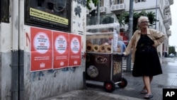 Seorang nenek penjual roti di sebelah poster bertuliskan "Tidak untuk proposal Uni Eropa, IMF dan ECB" di kota Thessaloniki, Yunani (1/7). (AP/Giannis Papanikos)