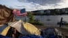 FILE - Frank, a homeless man, sits in his tent with a river view in Portland, Ore., on June 5, 2021. 