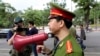 FILE - A Vietnamese police officer uses a speaker to order pedestrians including journalists to leave a closed area near the Chinese Embassy in Hanoi, Vietnam. 