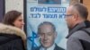 aption People look at a poster of Israel Prime Minister and governing Likud party leader Benjamin Netanyahu at a voting center in the northern Israeli city of Hadera, Dec. 26, 2019. 