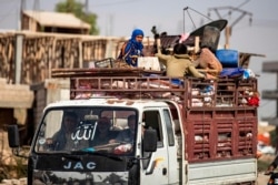 Displaced Syrians sit in the back of a pickup truck as Arab and Kurdish civilians flee amid Turkey's military assault on Kurdish-controlled areas in northeastern Syria, Oct. 11, 2019, in the Syrian border town of Tal Abyad.