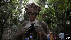 Wisatawan menunggu giliran untuk berfoto dengan patung figuratif yang berfungsi sebagai gapura karya seniman Afrika Selatan Daniel Popper berjudul, "Ven a la Luz" di resor Ahau Tulum, negara bagian Quintana Roo, Meksiko, Senin, 4 Januari, 2021. (AP Photo/Emilio Espejel)