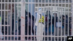 身穿防护服的工作人员看着从海外抵达北京的旅客进入北京国际会展中心等待接受进一步的健康甄别。（2020年3月18日）