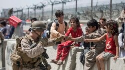 Watoto wakifurahi na mwanajeshi wa Marekani wakiwa uwanja wa ndege wa Kimataifa wa Hamid Karzai, Kabul, Afghanistan, Ijumaa Agosti 20, 2021, wakisubiri mchakato wa kuondolewa nchini kukamilika (Sgt. Samuel Ruiz/U.S. Marine Corps via AP)