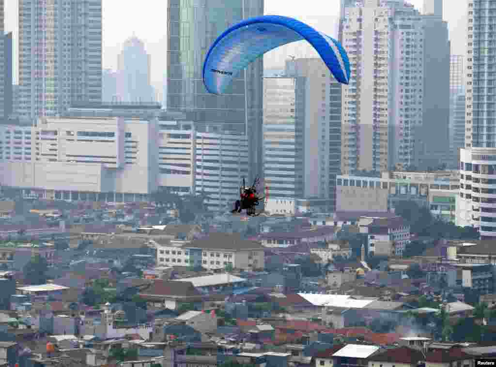 Seorang pilot mengemudikan paralayang (paraglider) saat terbang di atas Jakarta Pusat.