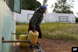 Joyce Mule fills jugs with water from a rock catchment system in Makueni County, Kenya on Thursday, Feb. 29, 2024. Villagers put big stones to filter the rainwater and a pipe to take the water down to storage tanks. (AP Photo/Brian Inganga)
