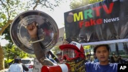 示威者在2021年2月11日星期四对缅甸曼德勒举行的军事政变抗议游行中，展示了谴责国家和军事电视台的标语牌。 