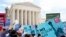 FILE - Protesters hold up signs outside the the Supreme Court in Washington, June 26, 2018.