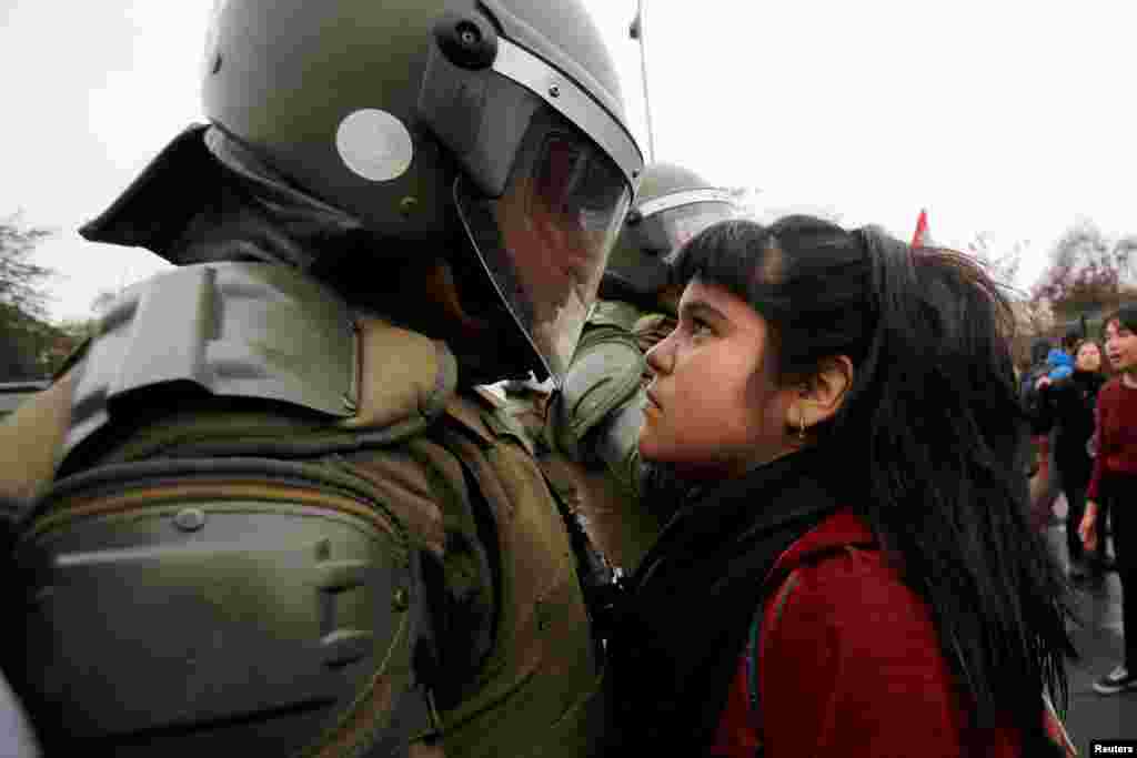 A demonstrator looks at a riot policeman during a protest marking the country's 1973 military coup in Santiago, Chile, Sept. 11, 2016.