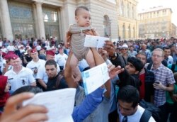 FILE - Migrants wave their train tickets and lift up children outside the main Eastern Railway station in Budapest, Hungary, Sept. 1, 2015.
