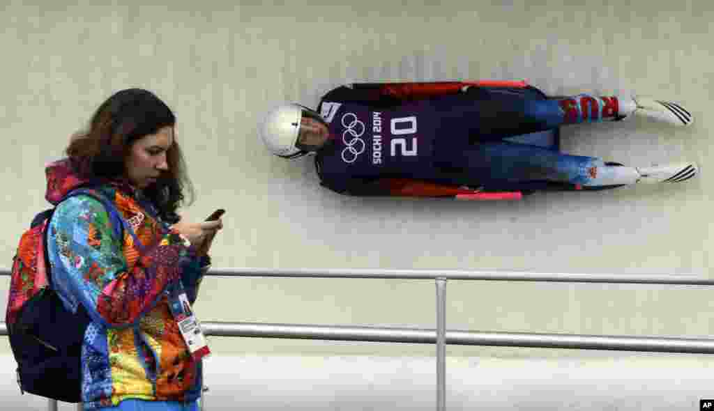 Natalja Khoreva dari Rusia pada latihan olahraga luging putri sementara seorang tenaga sukarela melewatinya di Krasnaya Polyana, Rusia (9/2). (AP/Dita Alangkara)