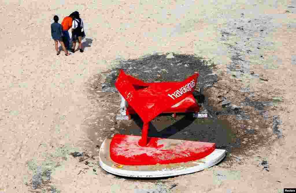 People stand near a sculpture that was damaged due to large waves, during the annual outdoor exhibition known as &quot;Sculpture by the Sea&quot; located on Tamarama Beach in Sydney, Australia.