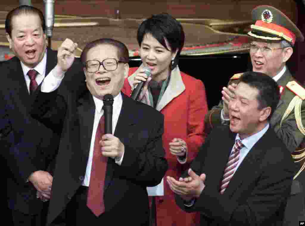 2000年12月20日，在澳门回归中国纪念仪式上，中国主席江泽民和副总理钱其琛（左）、解放军总政治部主任于永波（右后）、澳门特首何厚铧（右）等人同台唱歌。美联社的图片说明没说图上的女士是谁，貌似澳门赌王何鸿燊的四姨太梁安琪。