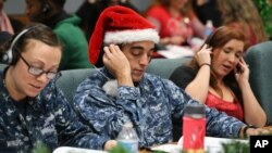 Santa tracker volunteers U.S. Navy Petty Officer Brandon Wright, center, and his wife, Petty Officer Emily Wright, left, take phone calls from children asking where Santa is and when he will deliver presents to their homes, inside a phone-in center during