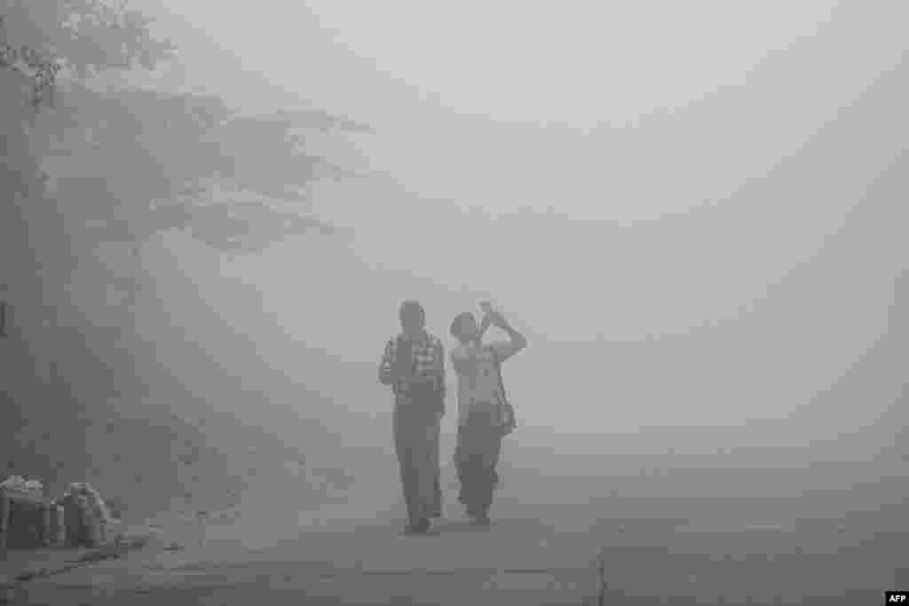 People walk along a residential street through early morning fog and high levels of air pollution in Yangon on February 14, 2025. (Photo by Sai Aung MAIN / AFP)