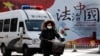 A woman and a police van pass a Chinese government propaganda billboard that reads "China Rule By Law" on a street in Beijing, Dec. 28, 2016. Infuriated by a decision by Beijing prosecutors to drop charges in a high-profile police brutality case, university alumni circles across China mobilized online this week with petition drives, posing to China's government an unusual challenge with its white-collar makeup and swiftly expanding nationwide reach. 