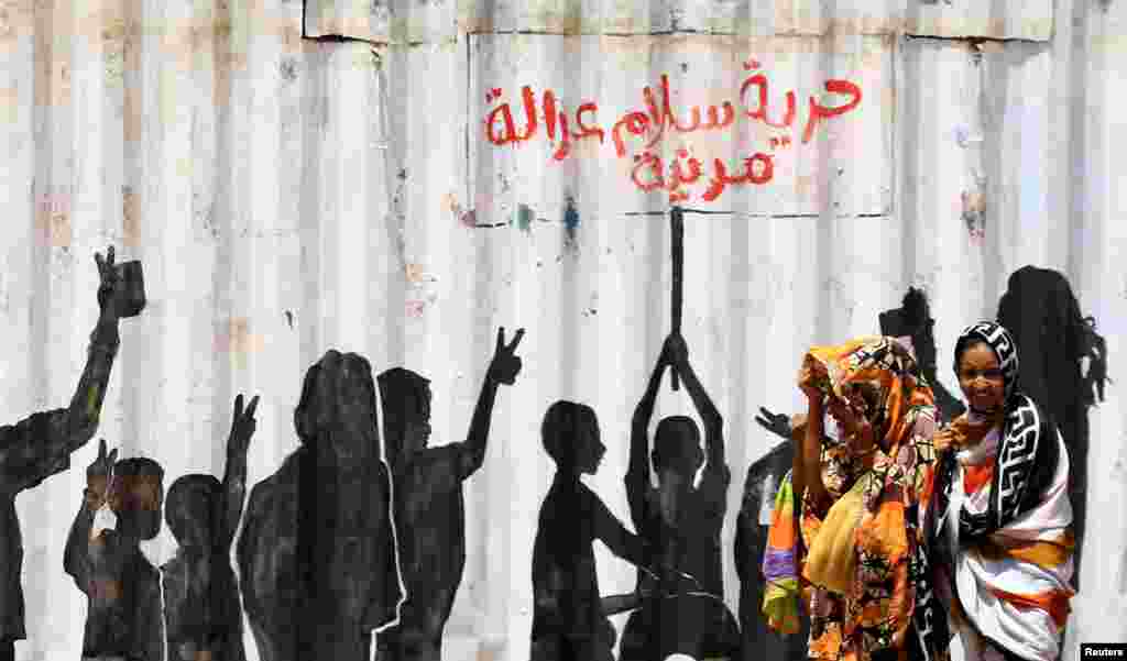 People walk past graffiti reading in Arabic &quot;Freedom, Peace, Justice and Civilian&quot; in the Burri district of Khartoum, Khartoum, Sudan.
