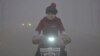 FILE - With a yellow smog alert in effect, a woman rides her electric bicycle along a street amid thick haze in Chiping county, Shandong province, China, Jan. 16, 2015.