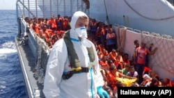 FILE - Migrants wait to be boarded on the San Giusto Navy ship, along the Mediterranean sea, off the Sicilian island of Lampedusa,, Aug. 23, 2014. 