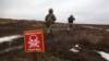 Ukrainian Military Forces servicemen walk past a metal plate which reads as "Caution mines" on the frontline with Russia-backed separatists near Luganske village, in Donetsk region, Jan. 11, 2022.