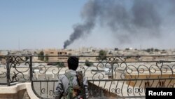 FILE - Seorang pejuang Kurdi dari unit People's protections melihat asap yang membumbung akibat serangan udara pasukan koalisi di Raqqa, Suriah. (16 Juni 2017)