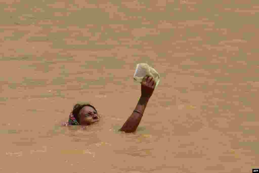 Seorang perempuan korban banjir memegang barangnya agar tidak basah saat mencoba untuk mencapai tempat yang lebih tinggi di pinggiran kota Patna, India.