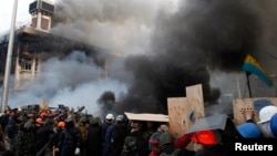 Para demonstran anti-pemerintah di Alun-Alun Kemerdekaan dekat gedung serikat perdagangan yang terbakar di pusat kota Kyiv (19/2). (Reuters/David Mdzinarishvili)