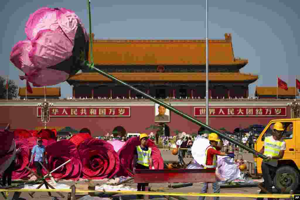 Workers guide an artificial flower blossom as it is lifted by crane for a large floral display under construction on Tiananmen Square in Beijing.