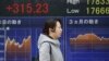 A woman walks by an electronic stock board of a securities firm in Tokyo, Feb. 1, 2016. Chinese stocks fell Monday after a weak manufacturing report. Other markets were mixed. 