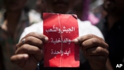 Seorang demonstran di Mesir memegang kertas bertuliskan "militer, masyarakat dan polisi -- satu tangan," dalam protes spontan menentang Presiden Mohammed Morsi di Alun-Alun Tahrir di Kairo (29/6). (AP/Manu Brabo)