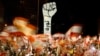 FILE - Protesters wave Lebanese flags during an anti-government protest in Beirut, Lebanon, Nov. 10, 2019. The Arabic writing beneath the fist reads "Revolution."