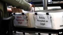 FILE - A Miami-Dade County Elections Department employee places a vote-by-mail ballot for the August 18 primary election into a box for rejected ballots at the Miami-Dade County Elections Department, in Doral, Florida, July 30, 2020.