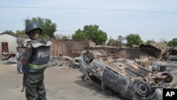 FILE - A Nigerian policeman stands guard by burned out cars and houses, following an attack by suspected Islamic extremists in Kawuri, Maiduguri, Nigeria.