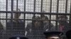 Policemen sit in front of a cage holding Egyptian employees of several pro-democracy groups during court proceedings in Cairo, Egypt, Sunday, February 26, 2012.