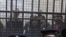 Policemen sit in front of a cage holding Egyptian employees of several pro-democracy groups during court proceedings in Cairo, Egypt, Sunday, February 26, 2012.