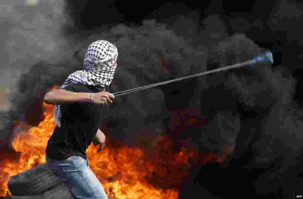 A Palestinian protester uses a slingshot to hurl stones towards Israeli security forces during clashes following a demonstration against the expropriation of Palestinian land by Israel.