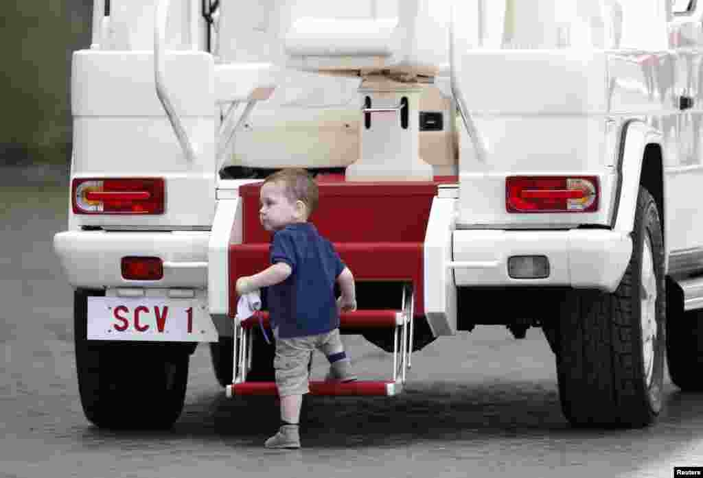 Seorang anak memanjat mobil Paus sementara Paus Fransiskus memimpin audiensi umum di lapangan Santo Petrus di Vatikan.