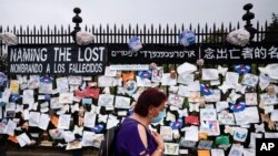 A woman passes a fence outside Brooklyn's Green-Wood Cemetery adorned with tributes to victims of COVID-19, May 28, 2020, in New York.