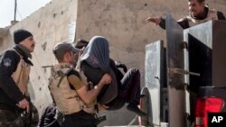 FILE - Iraqi security officers place a suspected Islamic State group member into the back of a waiting pickup truck, in east Mosul, Feb. 21, 2017.