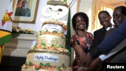 FILE: Zimbabwean President Robert Mugabe (R) is helped by his wife Grace (L) and son Chatunga (C) to cut a cake to celebrate his 92nd birthday at State House in Harare, Feb. 22, 2016. 